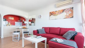 Una sala de estar moderna con un sofá rojo, una mesa de centro blanca y una zona de cocina con detalles en rojo.