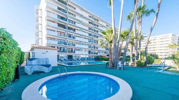 Un hotel con piscina, palmeras y un edificio de varios pisos con balcones.
