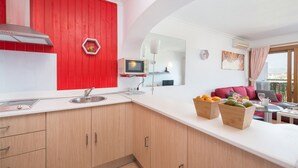 Una cocina moderna con una pared de acento roja, un microondas y un lavamanos. Hay un armario de madera con cajones y una encimera con un frutero.