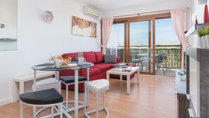 Un apartamento moderno con un sofá rojo, una mesita redonda y un balcón con vistas.