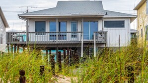 Ein zweistöckiges Haus mit Balkon, umgeben von hohem Gras und Sand.