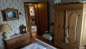 A bedroom with a bed, a wooden wardrobe, a dresser, a lamp, and a clock. - Large apartment / TLA with 3 room-kitchen-bathroom, terrace and balcony (120m²) (Landstuhl)