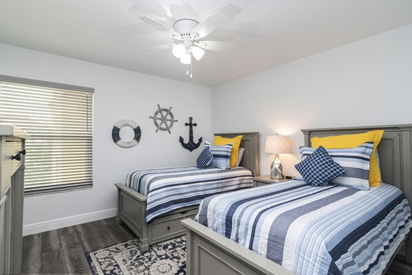 A bedroom with two beds, a ceiling fan, a ship's wheel, and a ship's anchor wall decor.