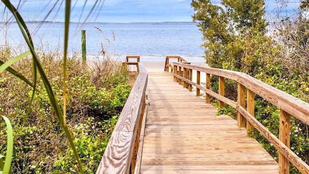 Une promenade en bois qui mène à une plage d’où l’on a une vue dégagée sur l’océan.