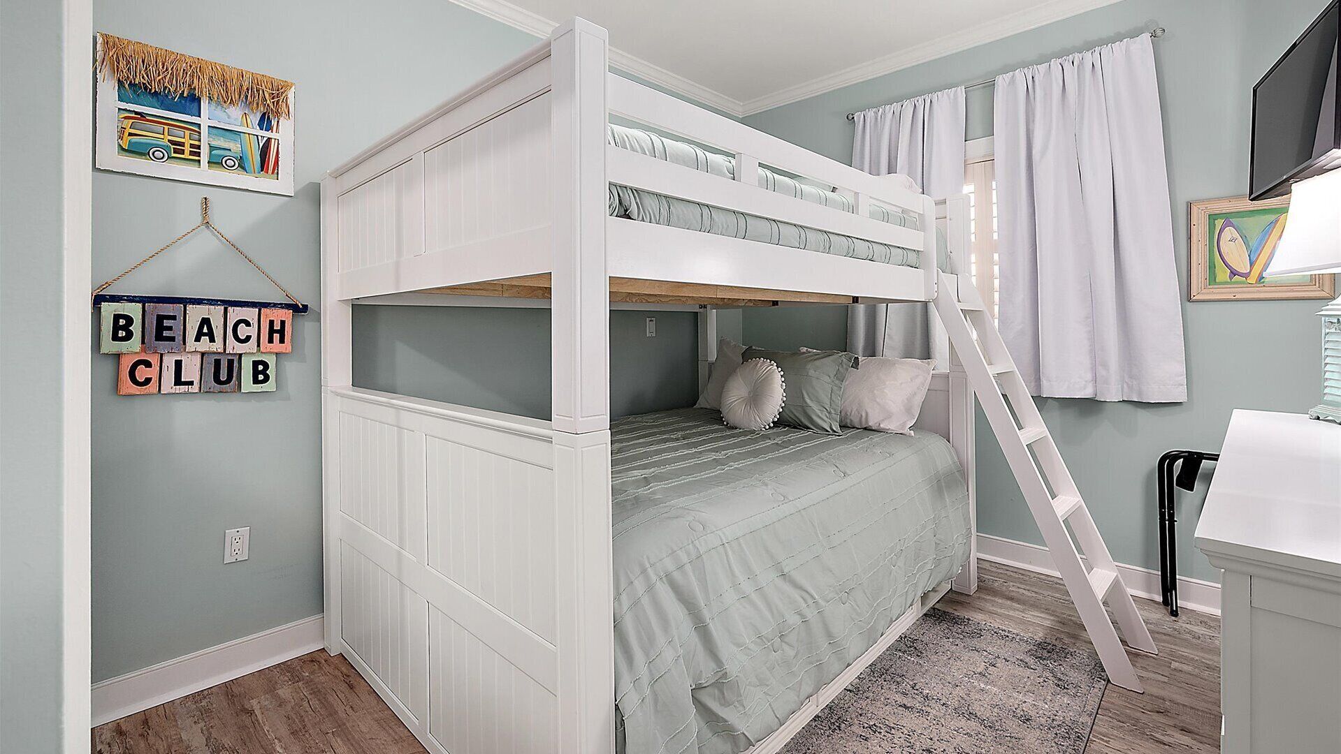 Habitación con literas, una escalera y un cartel que dice 'Beach Club', además de un cuadro en la pared.