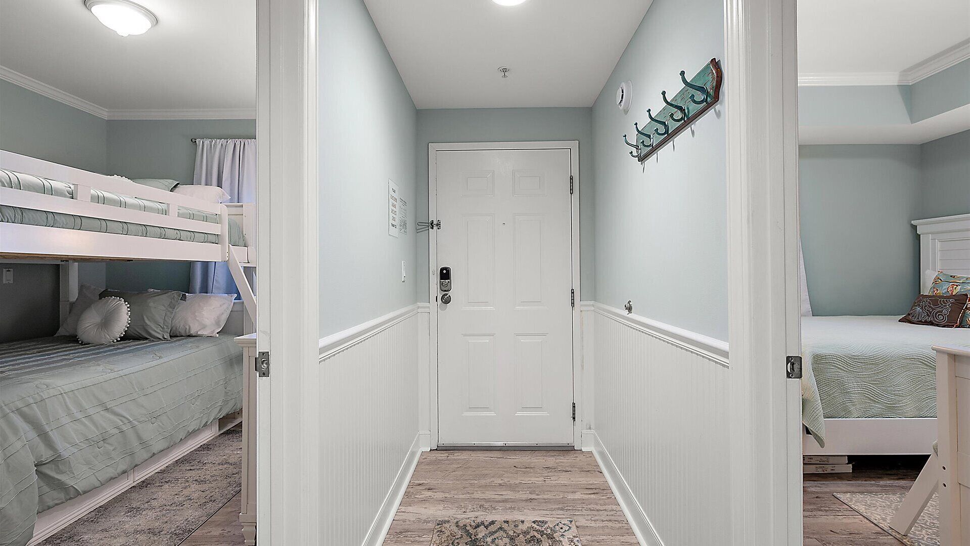 Un couloir étroit, avec une porte blanche au fond, et de part et d’autre, deux chambres équipées de lits superposés.
