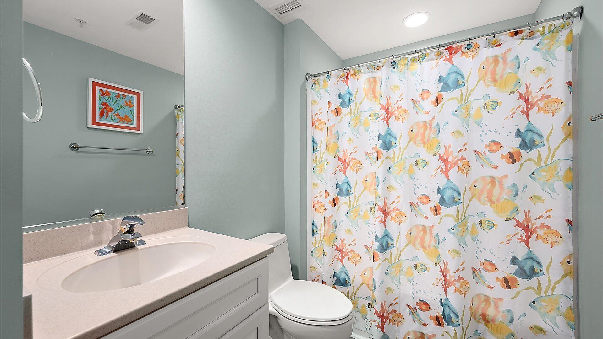 A bathroom with a sink, toilet, and shower curtain with a fish pattern.