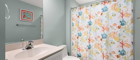 A bathroom with a sink, toilet, and shower curtain with a fish pattern.