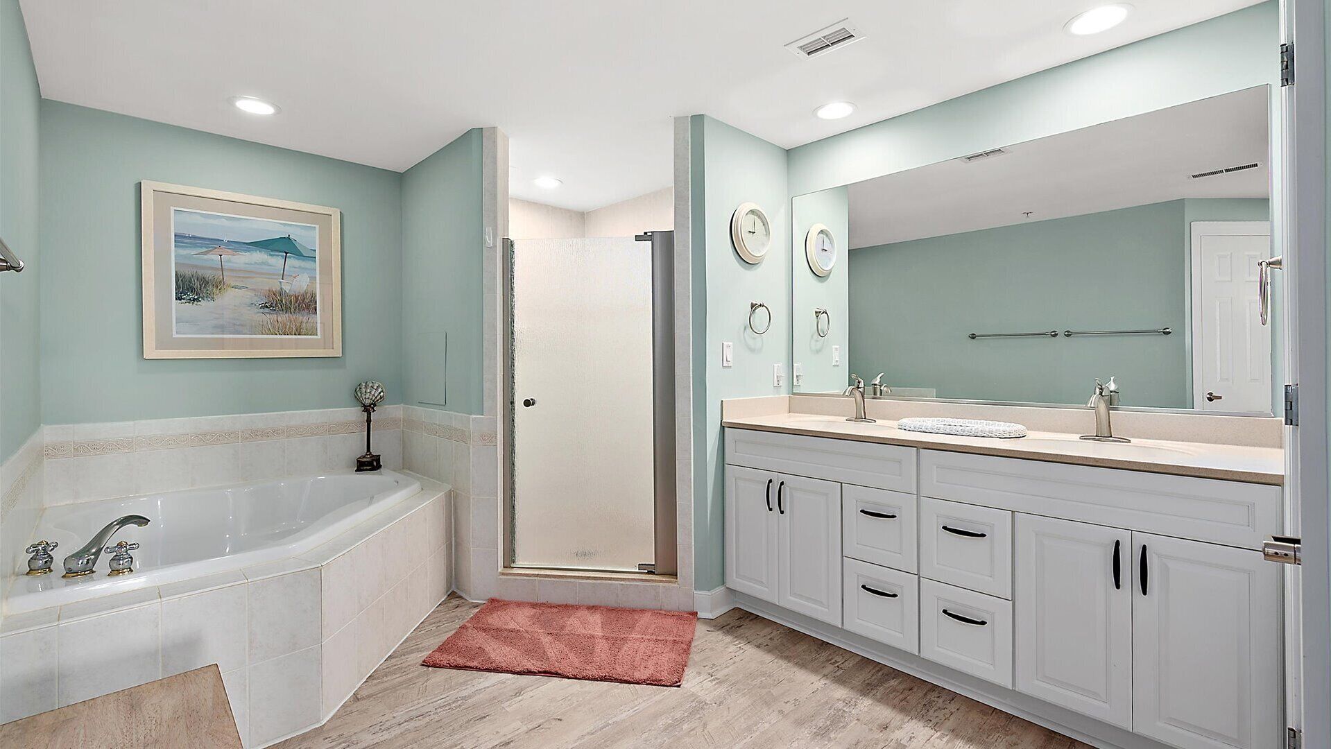 Une salle de bain avec une baignoire, une douche, un meuble-lavabo avec un miroir et un tableau encadré au mur.