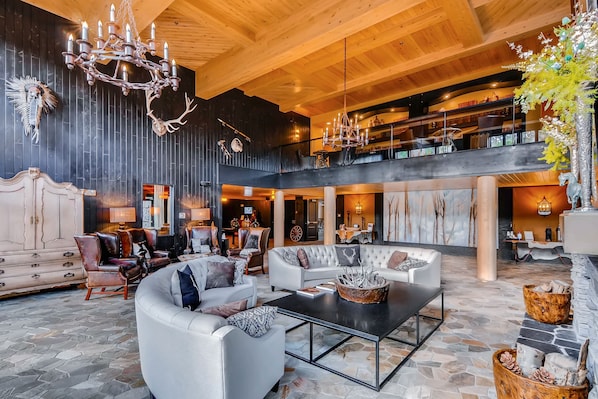 Relax in this elegantly furnished living area with a high ceiling and grand chandelier, featuring a plush sofa set and round coffee table.