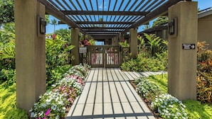 A covered walkway with a gate, surrounded by lush greenery and flowers.