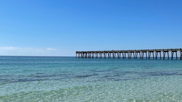 Una vista clara d'una platja amb un pont de fusta que s'endinsa al mar.