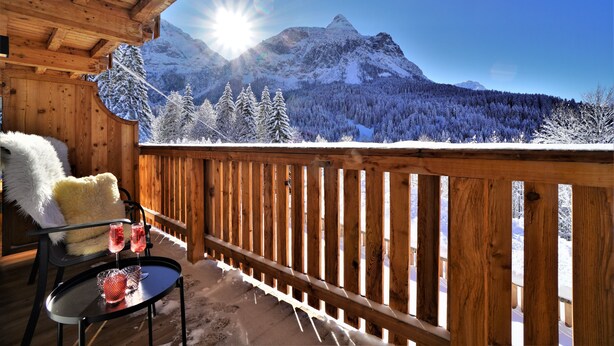 A wooden balcony with a view of snow-covered mountains and trees. - New Apart at the Zugspitze with spa, hot tub, barbecue area, beautiful outdoor area... (Ehrwald)