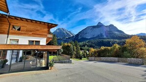 A modern building with large windows, a wooden facade, and a view of a mountain range. - New Apart at the Zugspitze with spa, hot tub, barbecue area, beautiful outdoor area... (Ehrwald)