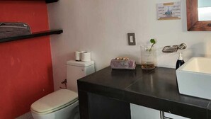 Un baño moderno con encimera negra, inodoro blanco y pared de acento roja.