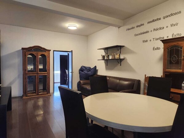 Un comedor con una mesa redonda, sillas, un aparador de madera y una pared con texto motivacional.