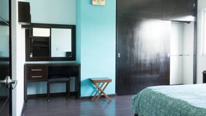 Un dormitorio con cama, escritorio con silla, una mesita, espejo y armario.