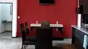 Ein Essbereich mit roter Akzentwand, einem flachbildfernseher über einem Tisch und einer Küche zur Rechten.