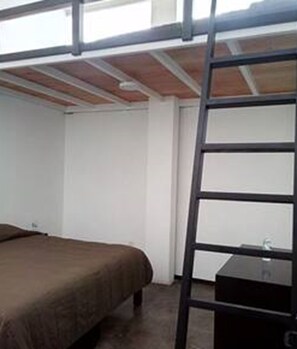 A bunk bed room with a ladder, a single bed, and a small black table.