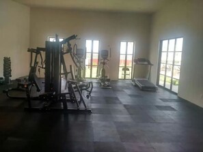 A gym with various exercise machines, a treadmill, and large windows allowing natural light.