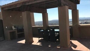 Un patio techado al aire libre con mesa y sillas, una parrilla y vistas del paisaje circundante.