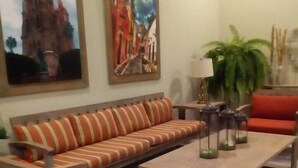 Una sala de estar con un sofá a rayas, sillones de madera, una mesita de centro y dos cuadros en la pared.