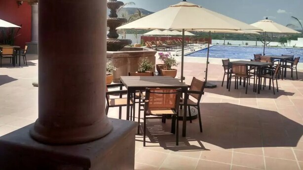 Un patio al aire libre con mesas, sillas, una piscina y sombrillas.