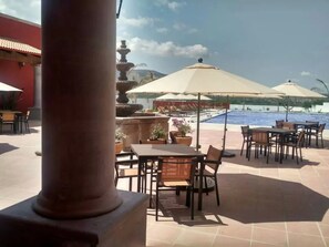 Une terrasse extérieure avec des tables et des chaises, une piscine et des parasols.