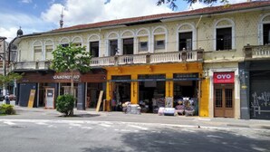 A street view of a building with a yellow facade, a visible balcony, and storefronts including a gas station and a hotel. - OYO Hotel Brás (São Paulo)