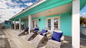 A covered wooden deck with Adirondack chairs and a teal-colored building. - Beautiful Crystal Beach Get Away - Close to everything. 3 BR - Sleeps 10 (Bolivar Peninsula)