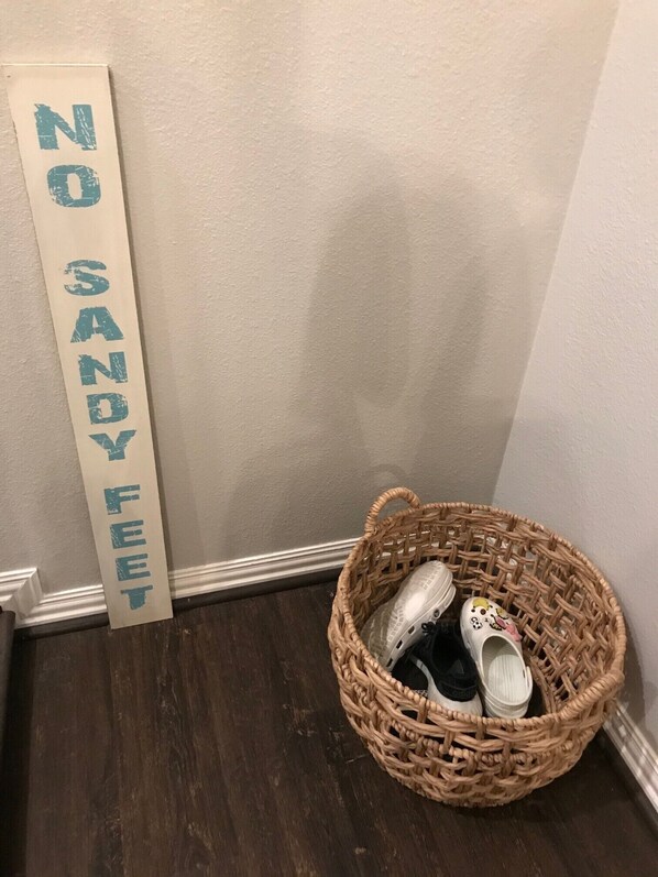 A corner with a 'NO SANDY FEET' sign and a wicker basket containing shoes.