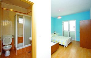 Two rooms with a bathroom featuring a toilet, shower, and sink, and a bedroom with a bed and window.