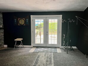 Una habitación con una puerta que da al exterior, un dardo, una silla y un juego de arco y flechas.