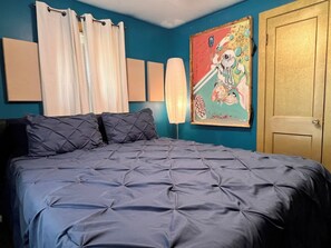 Un dormitorio con cama, cortinas, una lámpara de pared y una puerta.