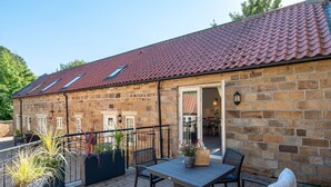 A stone building with a red-tiled roof, a balcony with wicker furniture, and potted plants. - Sandsend - Rambling Rose -  a family break that sleeps 4 guests  in 2 bedrooms (Whitby)