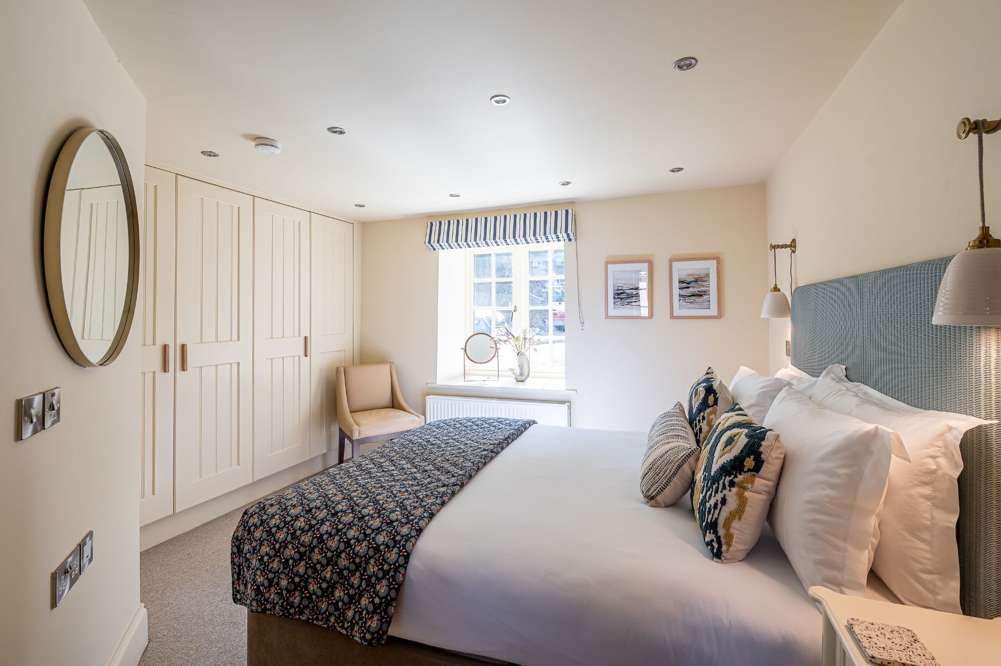 A bedroom with a bed, a chair, a wardrobe, a window with curtains, and a wall-mounted lamp.