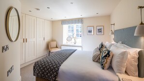 A bedroom with a bed, a chair, a wardrobe, a window with curtains, and a wall-mounted lamp. - Sandsend - Rambling Rose -  a family break that sleeps 4 guests  in 2 bedrooms (Whitby)