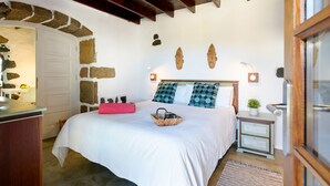 A bedroom with a stone archway, a bed with a white bedspread, two wall-mounted lamps, and a nightstand with a plant. - Hortensia, La Casa del Medianero (Macher)