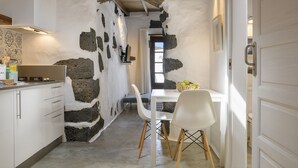 A kitchen with white cabinets, a stone wall, and a dining area with a white table and chairs. - Hortensia, La Casa del Medianero (Macher)