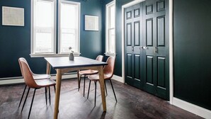 Een kamer met een donkergroene muur, een houten tafel met vier stoelen, en een deur met vier panelen.