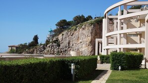 Un edificio moderno con fachada curva, una escalera que lleva a un balcón y un acantilado rocoso al fondo.