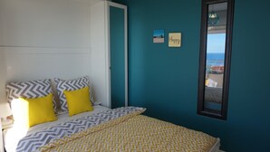 Un dormitorio con cama, dos almohadas, una mesita de noche, una ventana y vista al mar.
