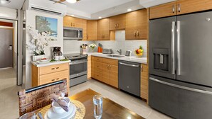 Cozinha moderna com armários de madeira, eletrodomésticos de aço inoxidável e um espaço de refeições com mesa posta para dois.