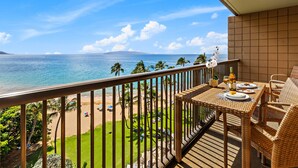 Uma varanda com vista para o oceano, uma mesa de jantar com cadeiras e um pequeno jardim.