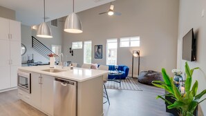 Amplia sala de estar con isla de cocina, un sofá azul y un ventanal que proporciona luz natural.