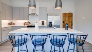 Una cocina moderna con una isla central, taburetes de bar y electrodomésticos de acero inoxidable.