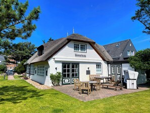 Un bâtiment traditionnel, de couleur blanche, avec un toit de chaume, une enseigne indiquant « Mummicham » et des tables et chaises en bois disposées à l’extérieur.