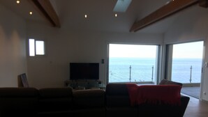 A living room with a large window overlooking the sea, a flat-screen TV, and a sofa. - Maison au Centre de Pietranera. Premier Étage (San-Martino-di-Lota)