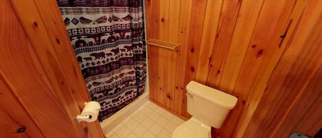 Un baño pequeño con paneles de madera, un inodoro, una cortina de ducha con estampados de animales y un dispensador de papel higiénico.