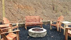 A circular fire pit surrounded by wooden Adirondack chairs and a stone wall.
